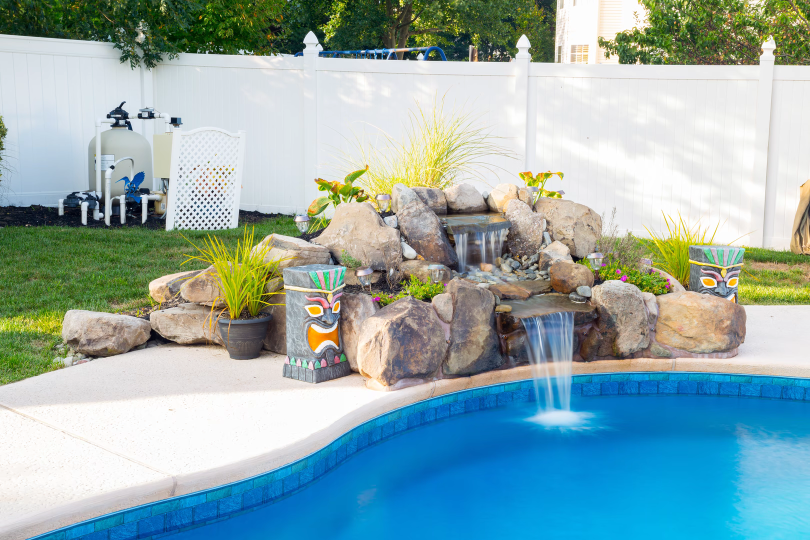 Two-tiered natural stone boulder waterfall cascading into a backyard pool with lush tropical plants