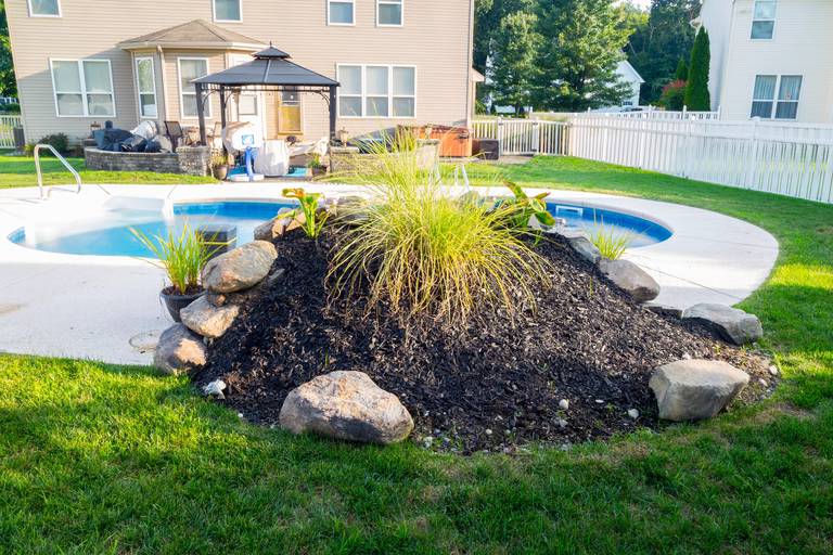 Natural stone boulder waterfall cascading into a backyard pool surrounded by vibrant ornamental grasses