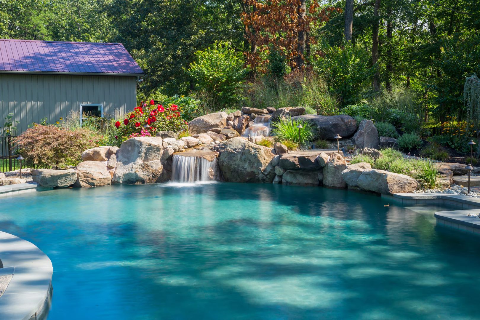 Two-tiered natural stone boulder waterfall cascading into a pool surrounded by lush garden plants