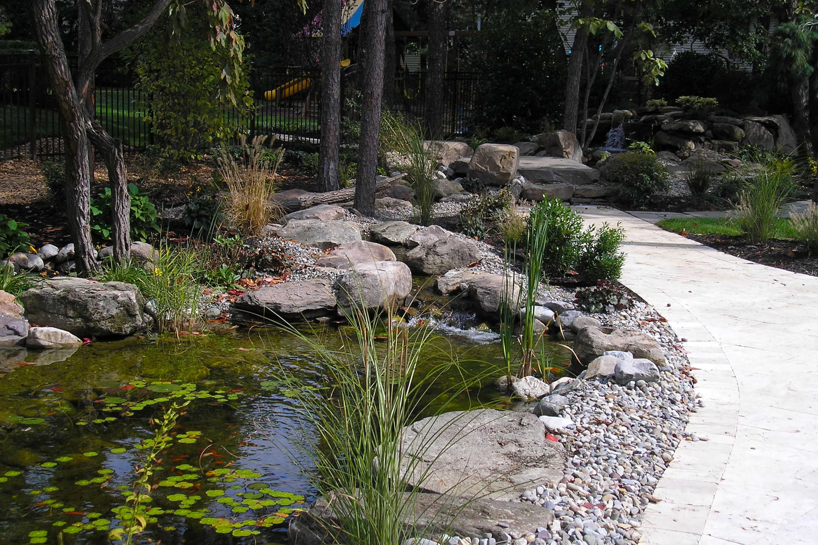 Cascading multi-tiered stone boulder waterfall flowing into a garden pond surrounded by lush plants