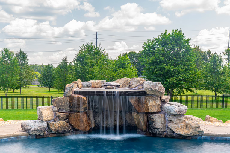 Natural stone boulder waterfall with curtain flow cascading into a pool near green trees