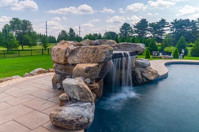 Comet D - Medford, NJ - A large rock waterfall in the middle of a swimming pool surrounded by lush green grass and trees