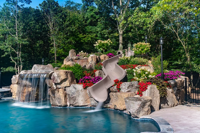 Copper C - Cream Ridge, NJ - A large rock garden with a water feature and a water slide, surrounded by lush greenery and colorful flowers