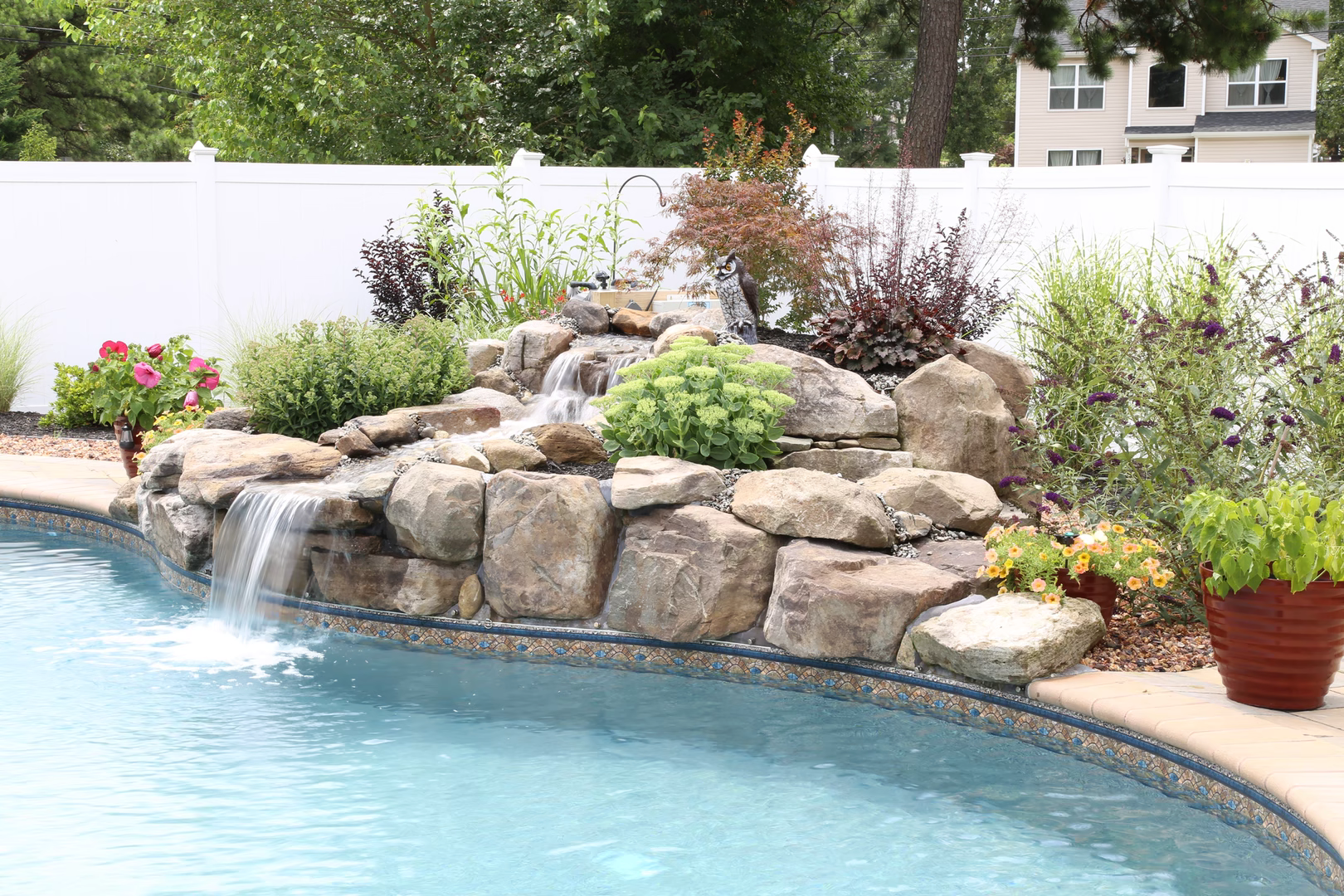 Natural stone boulder waterfall cascading into a pool surrounded by lush garden landscaping