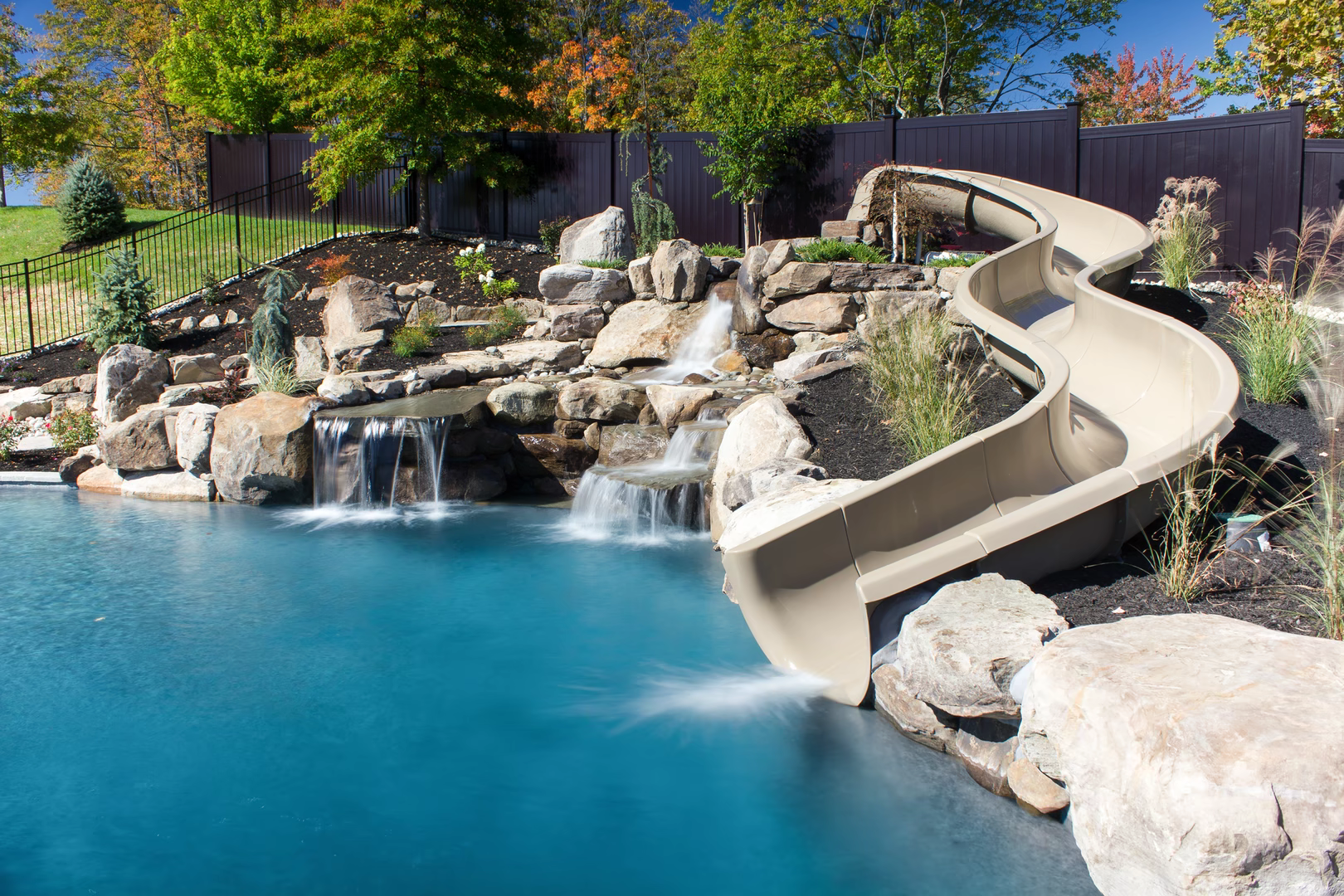 Multi-tiered natural stone boulder waterfalls cascading into a blue pool with lush garden landscaping
