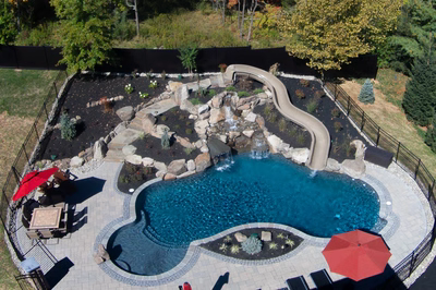 Crystal D - Flemington, NJ - A backyard with a swimming pool, waterfall, and patio area surrounded by trees