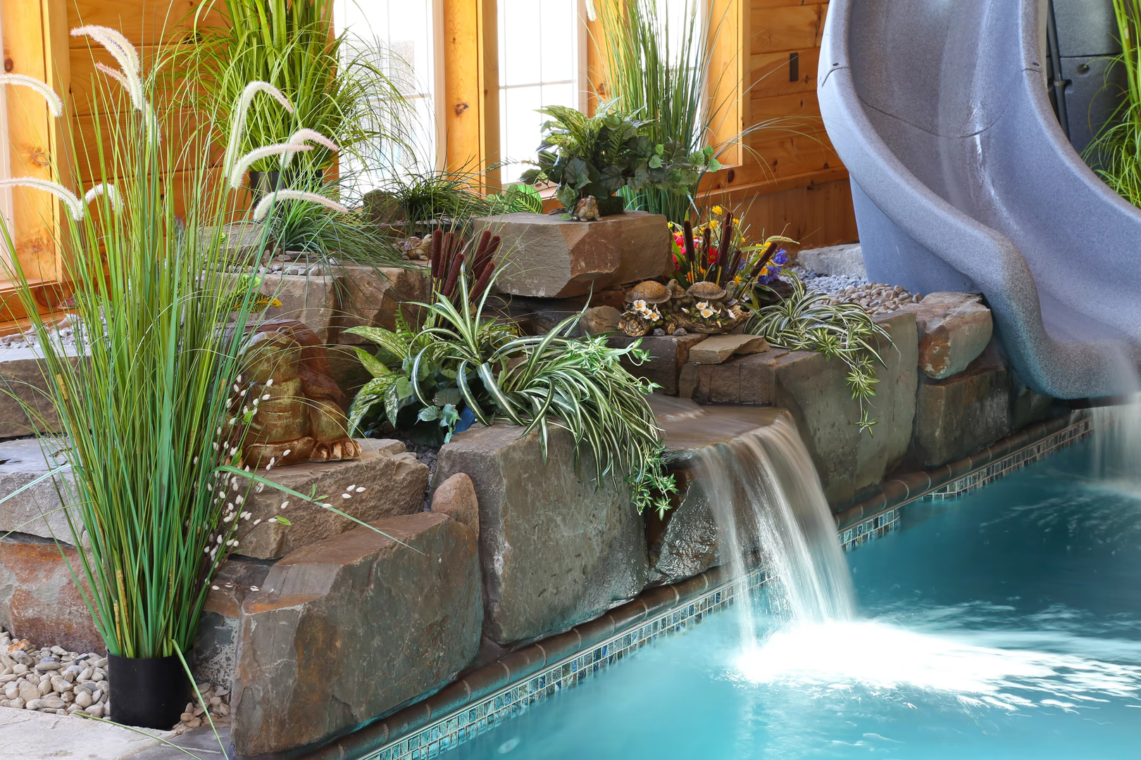 Tiered natural stone boulder waterfall cascading into a pool surrounded by lush indoor plants