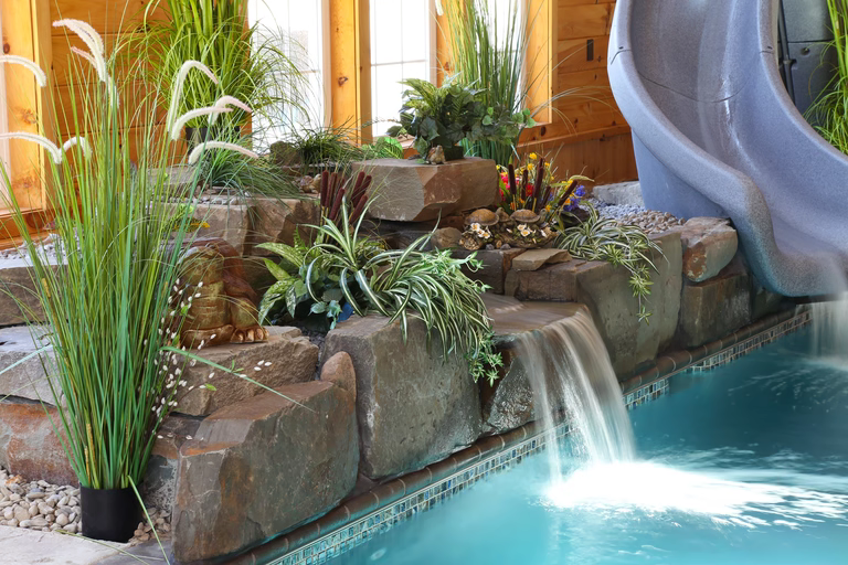 Tiered natural stone boulder waterfall cascading into a pool surrounded by lush indoor plants