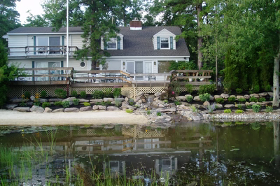 Dagg B - New Jersey - A large white house with a wooden deck next to a pond.