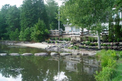 Dagg D - New Jersey - A house by a lake surrounded by trees and rocks.