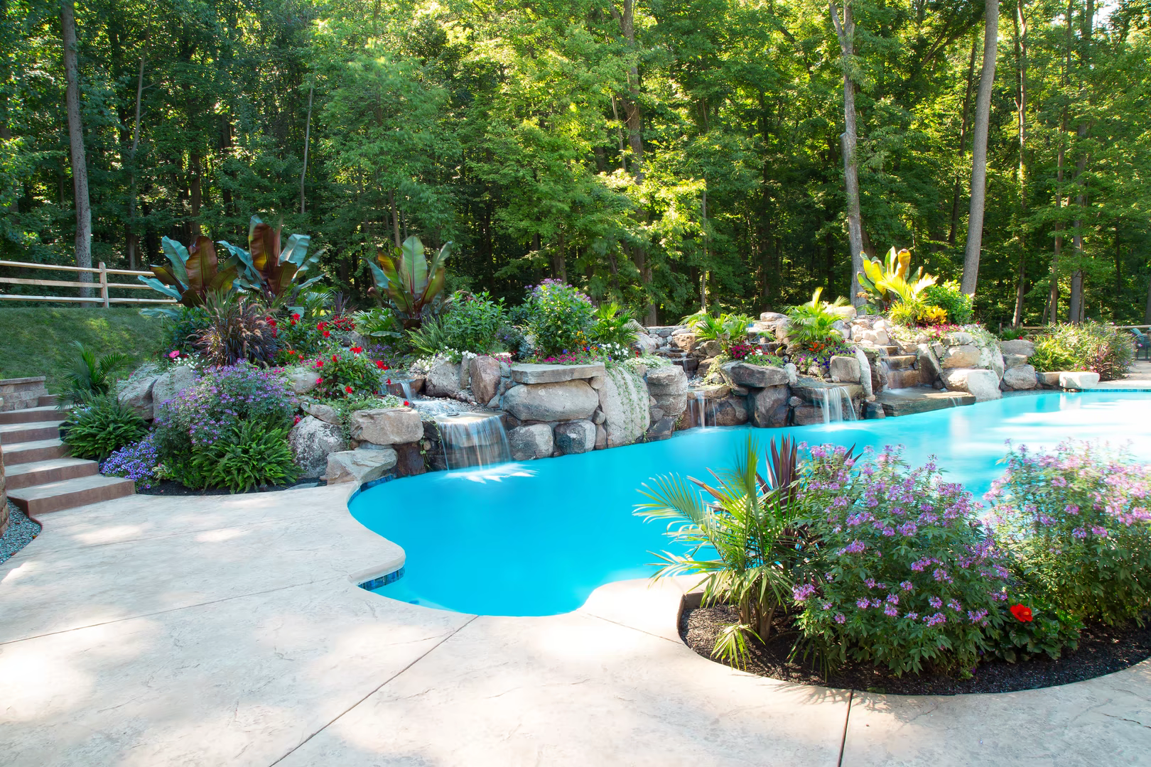 Multi-tiered natural stone boulder waterfalls cascading into a freeform pool with lush tropical landscaping