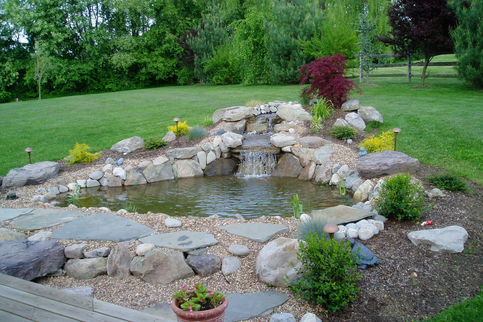 Natural stone boulder waterfall cascading into a garden pond surrounded by lush plants