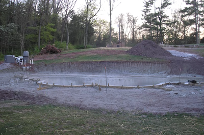 Dawa A - Bedminster, NJ - A construction site with a large concrete pool in the middle of a grassy area surrounded by trees