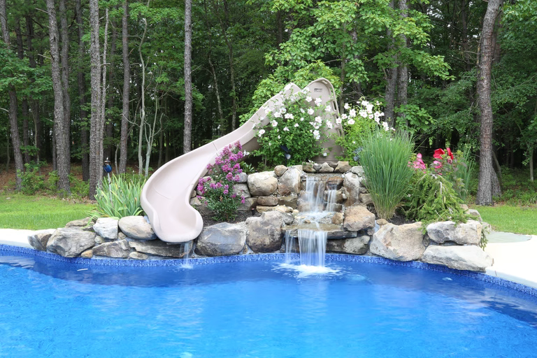Natural stone boulder waterfall cascading into a pool surrounded by lush garden plants