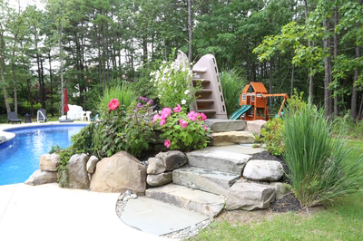 Dawson B - Jackson, NJ - A backyard with a swimming pool and a play structure surrounded by flowers and greenery