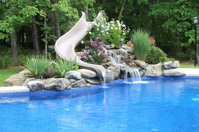 Dawson C - Jackson, NJ - A swimming pool with a water feature and a slide surrounded by flowers and greenery