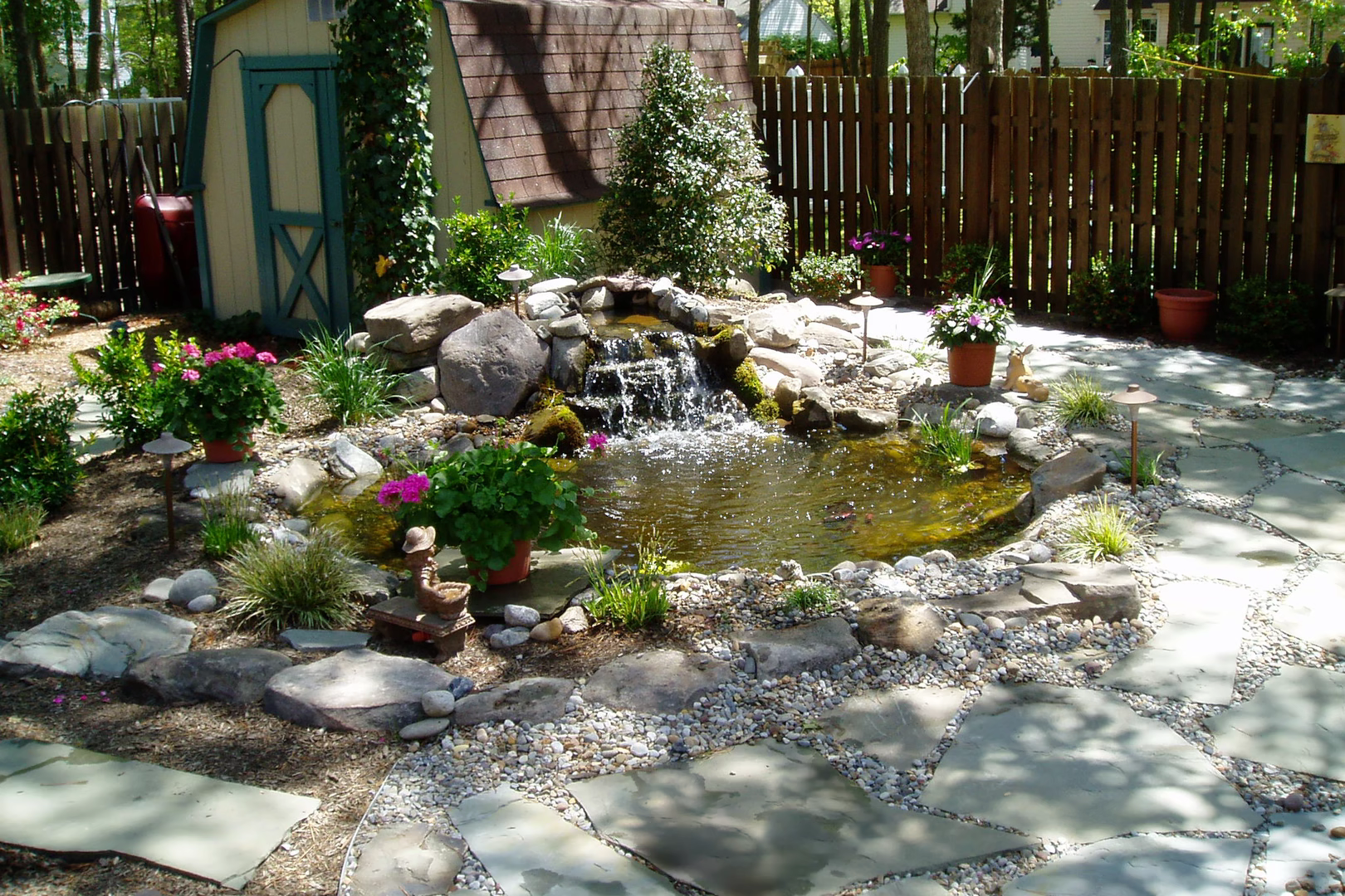 Natural stone boulder waterfall cascading into a garden pond surrounded by lush plants