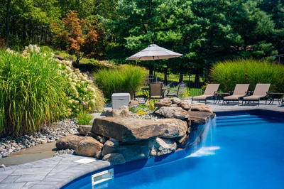 Decorah C - Wall, NJ - A swimming pool with a waterfall in the middle surrounded by lush greenery
