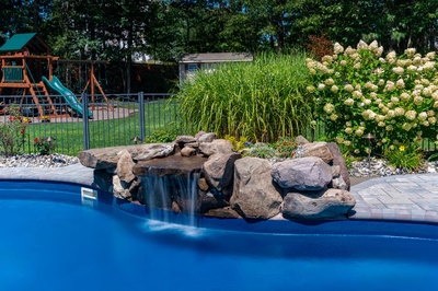 Decorah D - Wall, NJ - A backyard with a pool and a waterfall feature surrounded by flowers and greenery