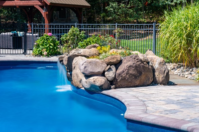 Decorah E - Wall, NJ - A blue swimming pool with a waterfall in the middle surrounded by rocks and plants