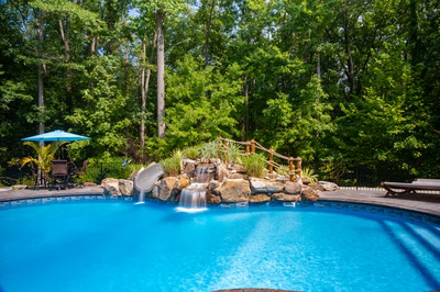 Desoto C - Perryville, MD - A blue swimming pool surrounded by lush green trees and a waterfall.