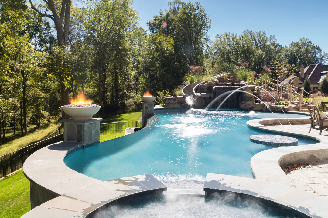 Dockett D - Ellicott City, MD - A swimming pool with a waterfall and fire pit surrounded by lush greenery