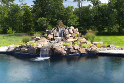 Drake A - Titusville, NJ - A large rock waterfall in the middle of a swimming pool surrounded by lush greenery
