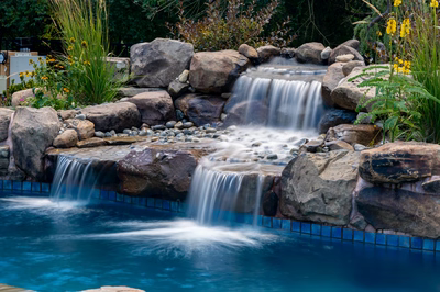 Elowah F - Collegeville, PA - A small waterfall cascades over rocks in a swimming pool surrounded by greenery and flowers