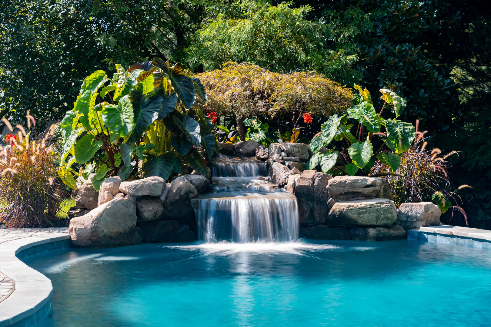 Natural stone boulder waterfall cascading into a pool surrounded by lush tropical landscaping