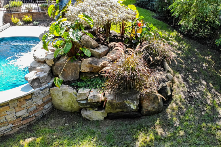 Natural stone boulder waterfall cascading into a pool with lush tropical garden surroundings