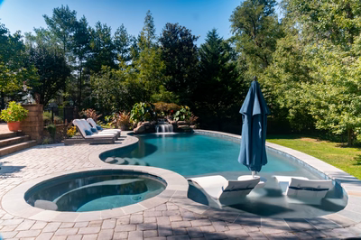Faxi E - Moorestown, NJ - A swimming pool surrounded by lush greenery and a waterfall, with lounge chairs and an umbrella