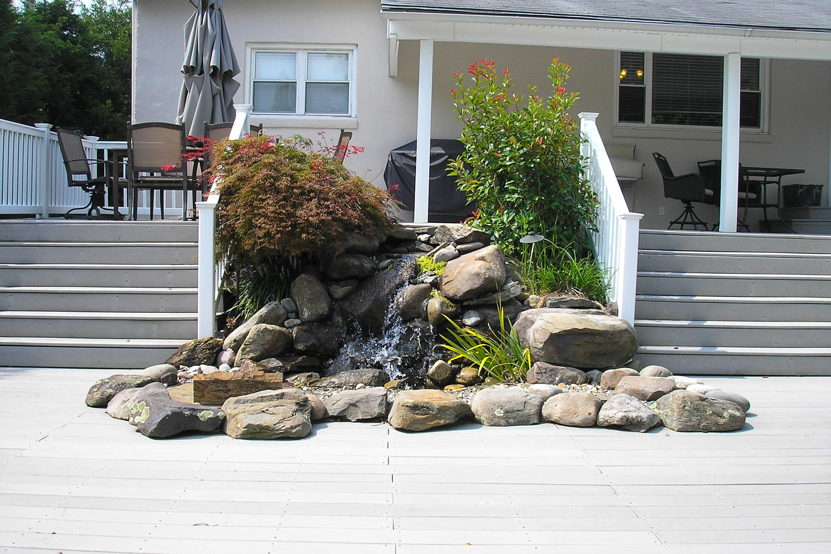 Natural stone boulder waterfall cascading into a basin surrounded by lush garden plants