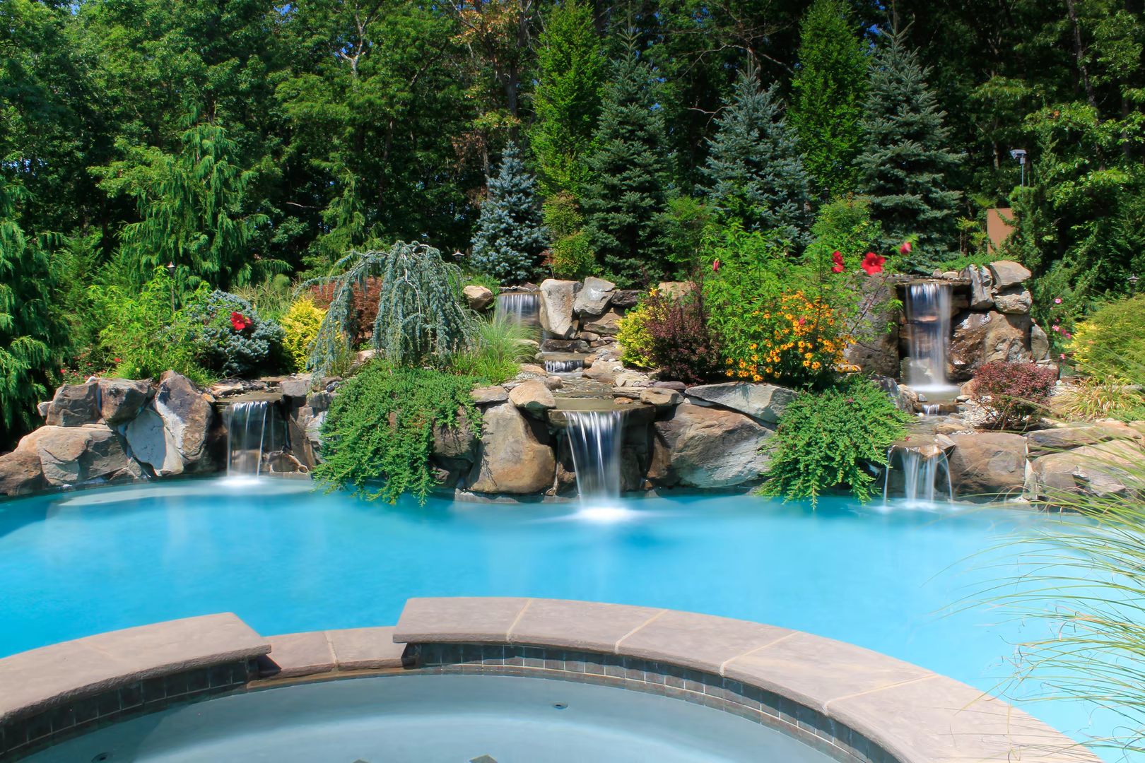 Natural stone boulder waterfalls cascading into a pool surrounded by lush garden landscaping