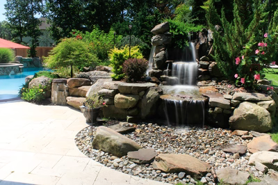 Flume F - Franklinville, NJ - A backyard with a waterfall and a pool surrounded by lush greenery and flowers