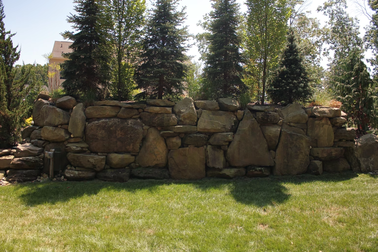 Natural stone boulder waterfall cascading into a backyard garden surrounded by tall evergreens