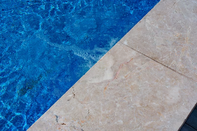 Formal B - Forrest Hills, MD - A close-up view of a blue swimming pool with clear water and a travertine edge