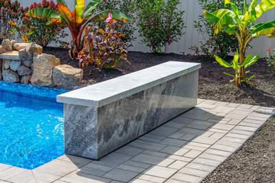 Formal G -  - A concrete bench sitting next to a swimming pool surrounded by tropical plants