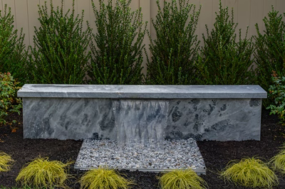 Formal G -  - A concrete bench with a waterfall in a garden setting surrounded by shrubs and grasses