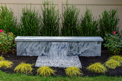 Formal G -  - A concrete bench with a waterfall in a garden setting surrounded by plants and flowers