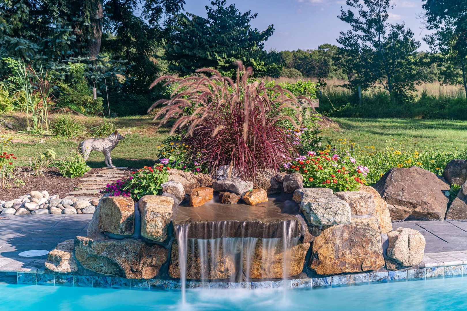 Single-tier natural stone boulder waterfall cascading into a pool surrounded by lush garden plants