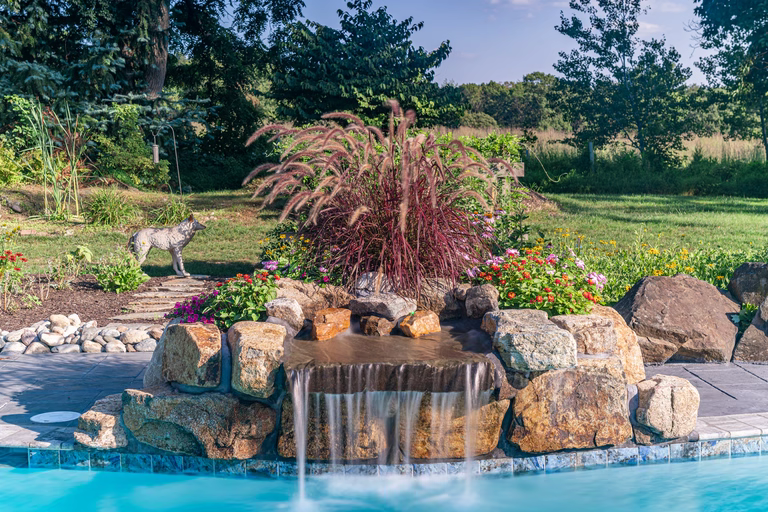 Natural stone boulder waterfall cascading into a pool surrounded by lush garden plants
