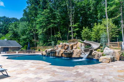 Gavarnie E - Monkton, MD - A swimming pool with a waterfall and a slide surrounded by lush greenery