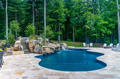 Gavarnie F - Monkton, MD - A swimming pool surrounded by lush green trees and a stone waterfall.