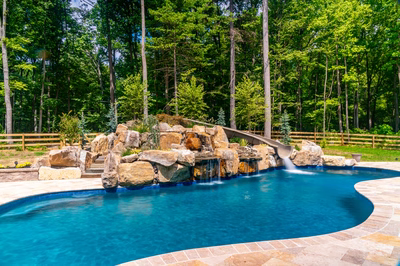 Gavarnie G - Monkton, MD - A swimming pool with a waterfall and a slide surrounded by lush green trees