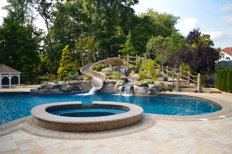 Natural stone boulder waterfall cascading into a freeform pool with lush surrounding landscaping