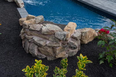 Genesis C -  - A rock waterfall in the middle of a swimming pool surrounded by plants and flowers