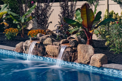 Genesis D -  - A swimming pool with a waterfall surrounded by tropical plants and flowers