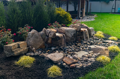 Genesis D - A garden with a small waterfall surrounded by rocks and plants