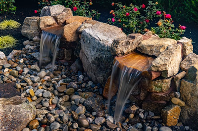 Genesis D - A small waterfall surrounded by rocks and pebbles in a garden setting