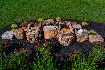 Genesis D - A stone structure surrounded by flowers and grass in a garden setting
